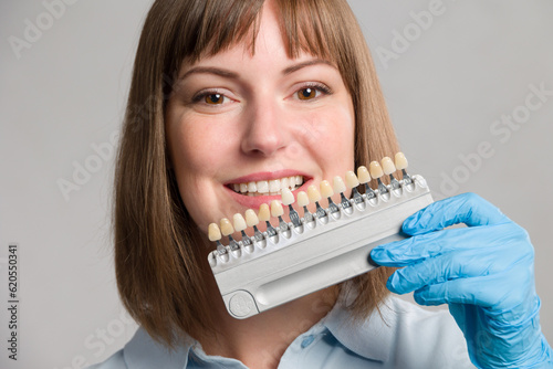 Close-up of dentist using shade guide at woman's mouth to check veneer of teeth for bleaching