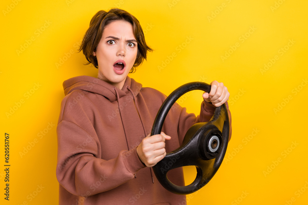 Portrait of impressed girl bob hair dressed brown sportswear astonished staring hold steering wheel isolated on yellow color background Portrait of impressed girl bob hair dressed brown sportswear astonished staring hold steering wheel isolated on yellow color background