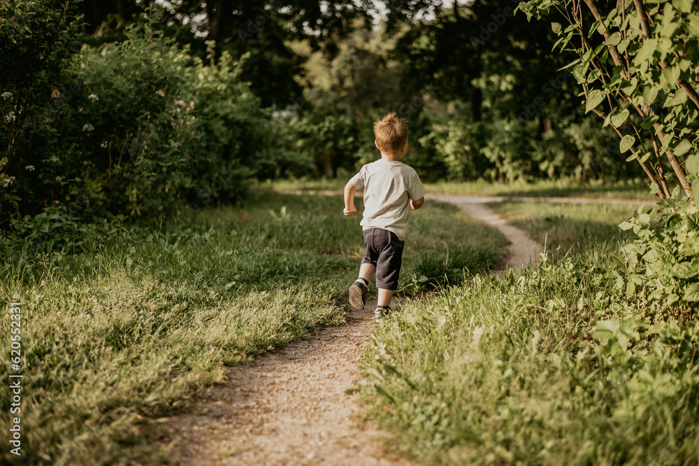 A little boy joyfully runs through the green grass in the summer in the park along a narrow path and smiles happily A little boy joyfully runs through the green grass in the summer in the park along a narrow path and smiles happily