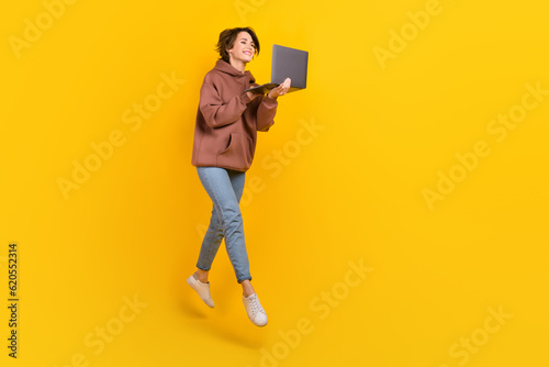 Full body portrait of excited cheerful lady jumping use netbook empty space isolated on yellow color background