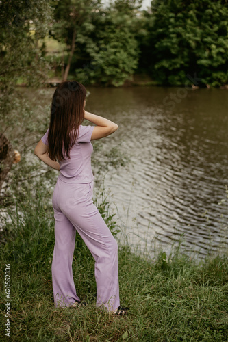 a girl in a lilac suit stands on the shore of a pond in summer. a walk in the park. © Мария Житная