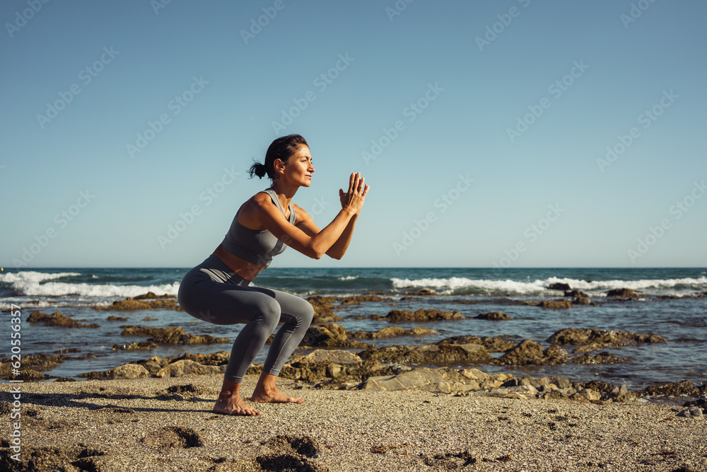 a beautiful brunette girl in gray leggings is engaged in fitness on the sand against the background of the sea a beautiful brunette girl in gray leggings is engaged in fitness on the sand against the background of the sea