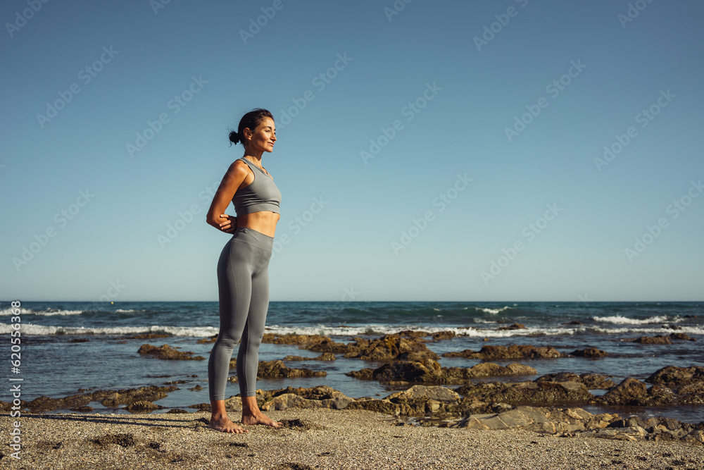 a beautiful brunette girl in gray leggings is engaged in fitness on the sand against the background of the sea