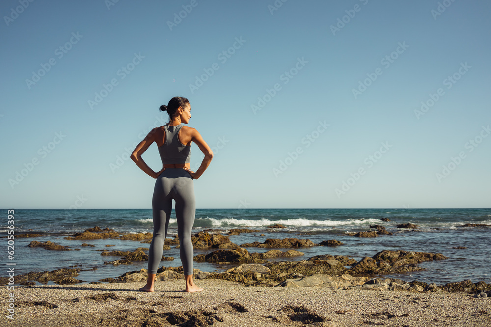 a beautiful brunette girl in gray leggings is engaged in fitness on the sand against the background of the sea