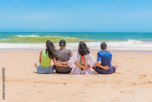 Família sentada na areia da praia de costas e abraçados