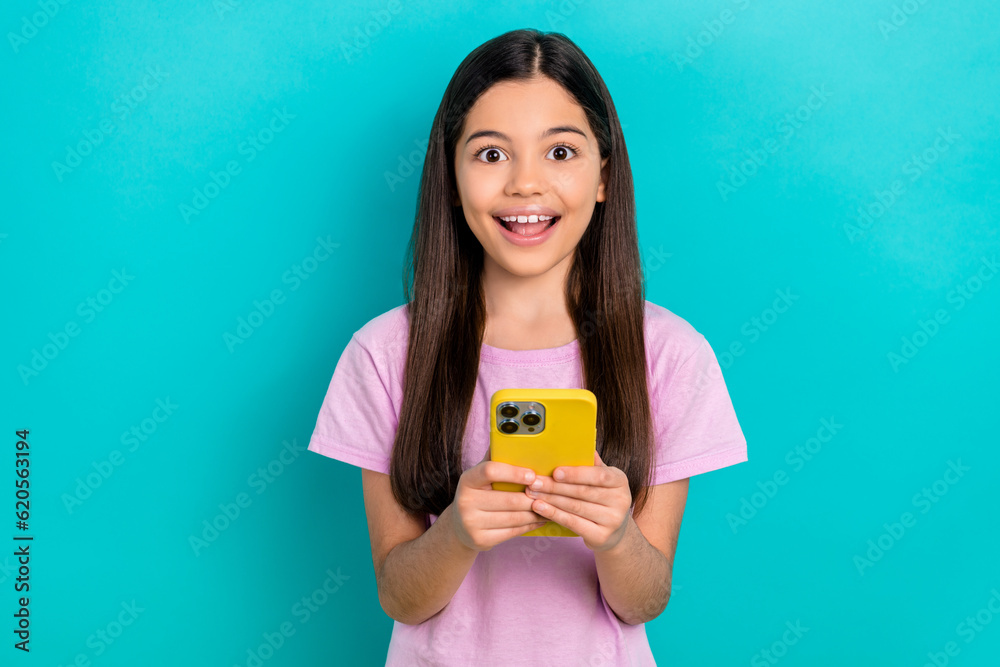 Photo of positive excited small kid wear pink t-shirt reading modern gadget isolated turquoise color background