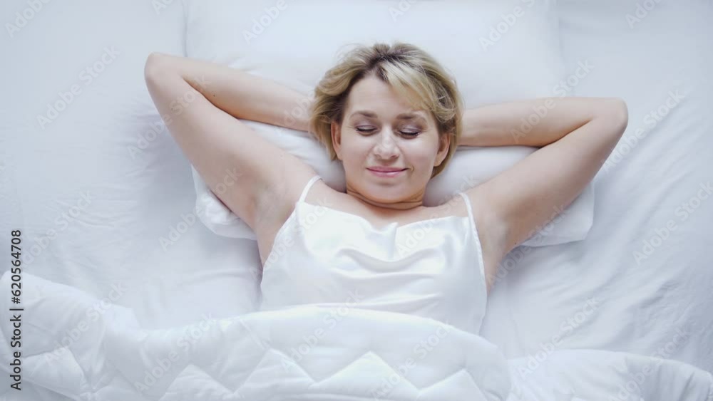 Cheerful attractive woman waking up in cozy bed with fresh white bedding, enjoying perfect sleeping quality on orthopedic pillow and mattress, top-view Cheerful attractive woman waking up in cozy bed with fresh white bedding, enjoying perfect sleeping quality on orthopedic pillow and mattress, top-view