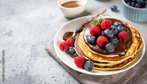 Pancakes with raspberries and blueberries and chocolate sauce for breakfast, on a concrete light background