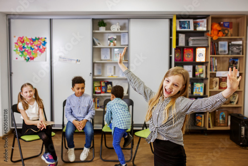 Schoolgirl standing in middle of classroom and answering question in front of classmates and teacher