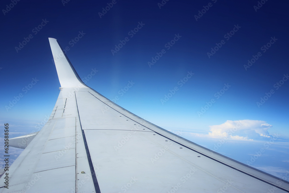 View of wing of an airplane through the window, against a blue sky and clouds View of wing of an airplane through the window, against a blue sky and clouds