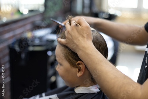 The hairdresser's hands professionally trit the child's hair. The hairdresser combs the hair on the renka's head and cuts off the regrown ends. The concept of a child in a barbershop.