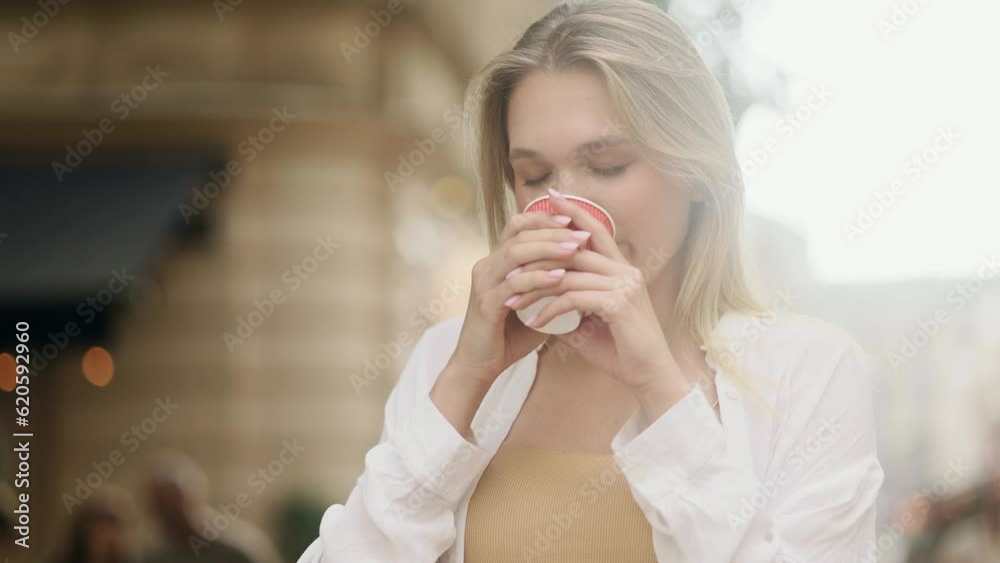 Close up portrait of charming blond woman enjoying cup of coffee or tea outdoors Pretty smiling girl relaxing at city street alone Beautiful day concept Close up portrait of charming blond woman enjoying cup of coffee or tea outdoors Pretty smiling girl relaxing at city street alone Beautiful day concept
