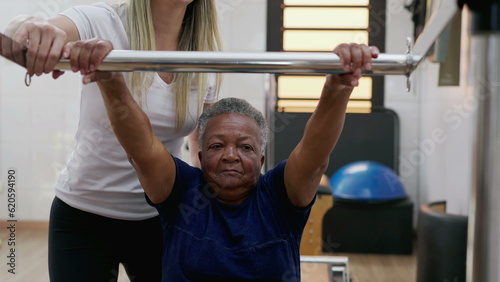 Female Pilates Coach assisting a black senior woman to use machine, old age workout routine, flexibility and strengthening body