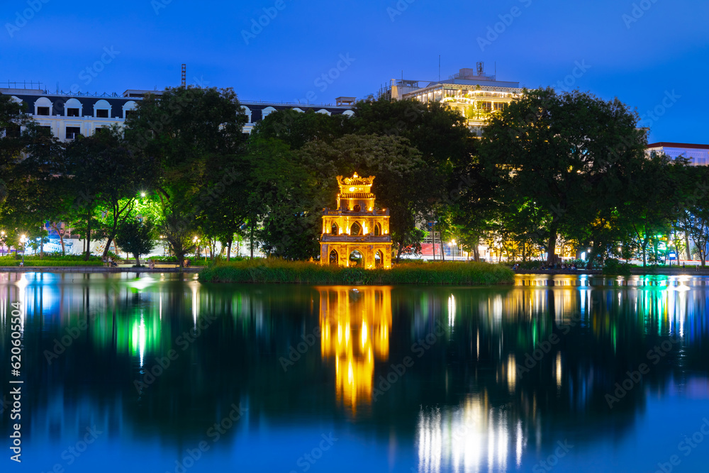 Hanoi City Old Quarters Lake at night glowing with vibrant colourful city lights surrounded by old historic buildings small bridge crossing the lake into a temple on a small island Hanoi Vietnam