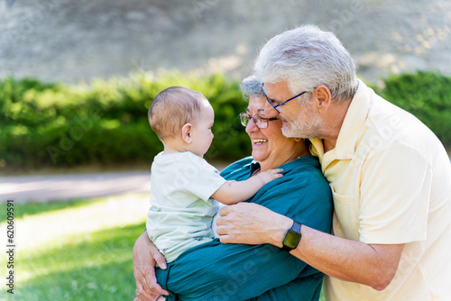 Fotografie Smiling grandparents looking at their baby grandson while holding him in their a
