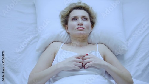 Woman lying in her bed in morning, waking-up and contemplating about plans for a day, has no mood to get-up