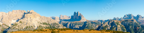 Panoramic over beautiful magical Three Dolomite peaks at the national park Three Peaks, Tre Cime Drei Zinnen in Autumn colors at blue sky and sunny day, South Tyrol, Italy
