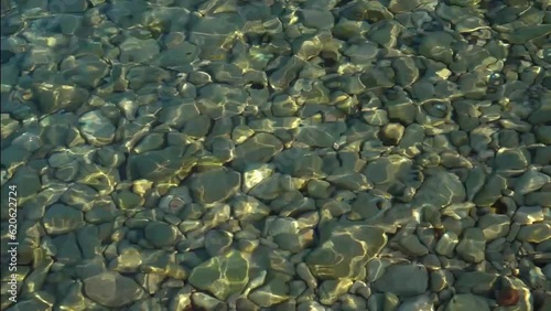 Medium-sized pebbles at the bottom of the seaSeashore with emerald water. Quiet summer evening. Sunset