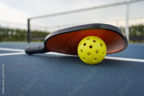 Pickleball paddle with pickleball with net in background. photo