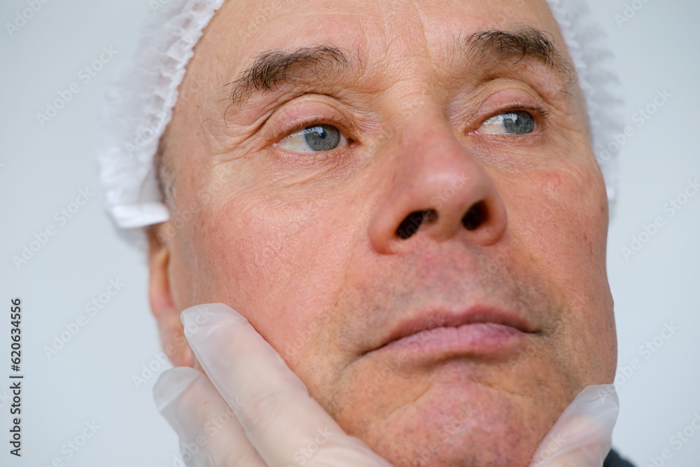 Obraz premium mature male face, man 60-65 years old years old, doctor, beautician, cosmetologist examines wrinkles, skin, age-related changes concept, aesthetic injection cosmetology, care anti-aging procedures