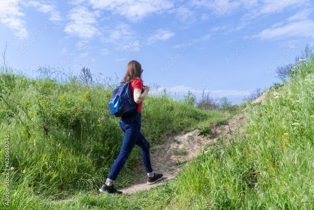 Tourist woman with backpack walking in deciduous forest. Active adult leisure of hiking in green valley. Person enjoy wanderlust and view of the spring grassy hill. Female hiker explore of wildlife. Tourist woman with backpack walking in deciduous forest. Active adult leisure of hiking in green valley. Person enjoy wanderlust and view of the spring grassy hill. Female hiker explore of wildlife.