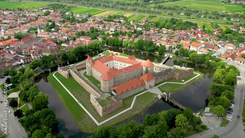 Cinematic aerial perspective of Fagaras city, with Fagaras Fortress in the middle, surrounded by water. Beautiful travel destination in Romania. Drone spinning around the fortress , descending