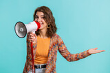 Woman talking with megaphone, proclaiming news, loudly announcing advertisement, warning using loudspeaker to shout speech, pointing empty place. Copy-space. Pretty brunette girl on blue background