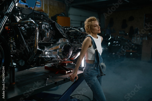 Young blond woman mechanic at motorcycle workshop side view shot