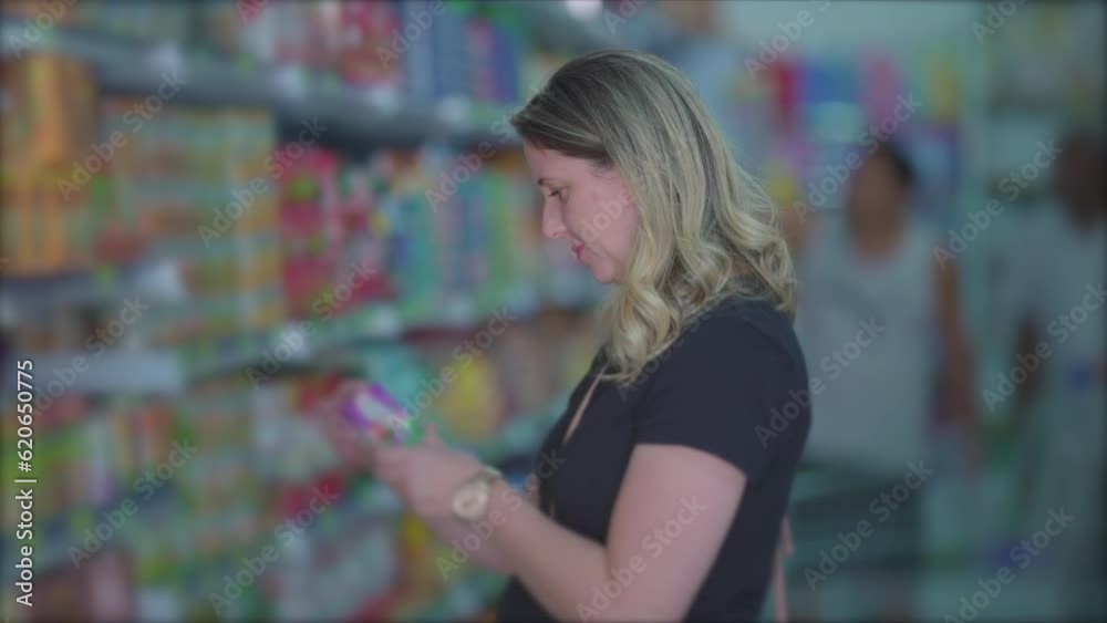 Female grocery shopping looking at item from shelf standing inside aisle, woman reading product label Female grocery shopping looking at item from shelf standing inside aisle, woman reading product label