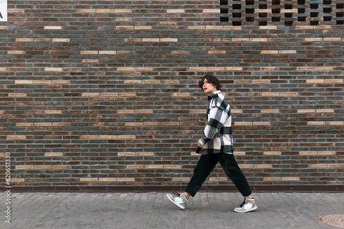 young man walks down the street in front of a brick wall
