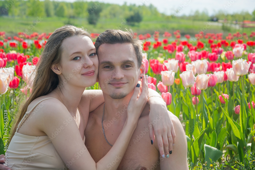 Young beautiful smiling couple sits on the background of a field of colorful tulips.