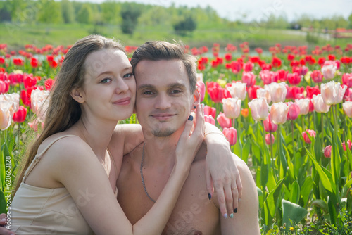 Obraz na płótnie Young beautiful smiling couple sits on the background of a field of colorful tulips. w salonie