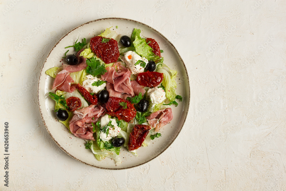 salad with dried tomatoes, prosciutto, soft cheese, olives, homemade, top view,