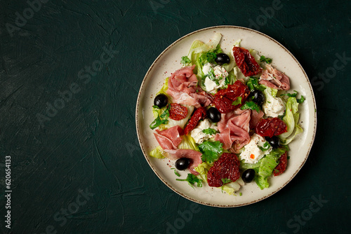 salad with dried tomatoes, prosciutto, soft cheese, olives, homemade, top view,