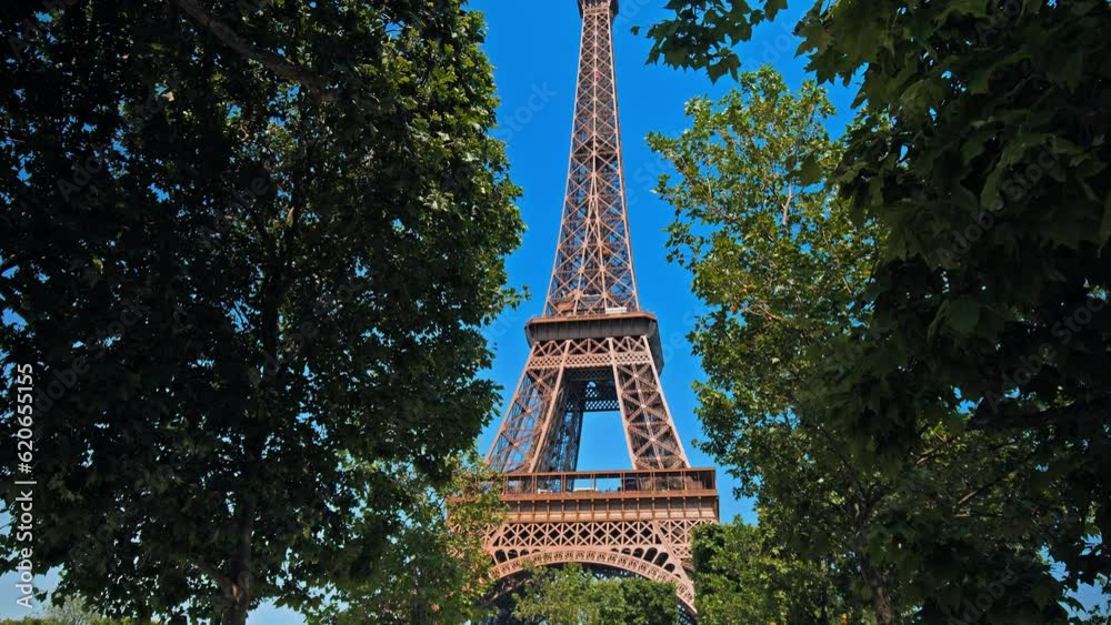 Close-up view of the Tower's detailed wrought-iron structure of the historical landmark in Paris. Amazing view of the Tour between green trees of the World famous symbol of Paris on a sunny day.