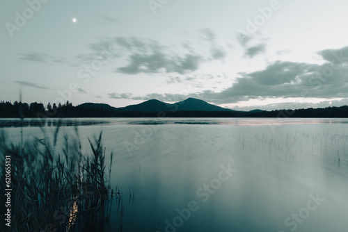 Fototapeta Naklejka Na Ścianę i Meble -  vue de deux sommet de montagnes au loin de l'autre côté du lac la nuit avec des petits nuages qui flottent dans le ciel
