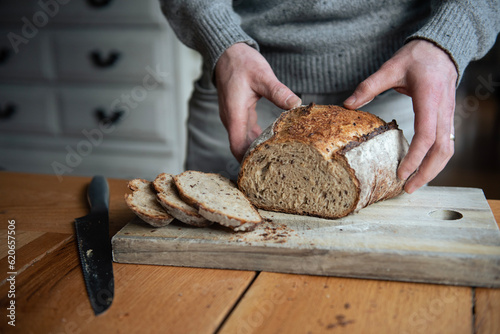 Man in sweater cutting sourdough bread at kitchen table