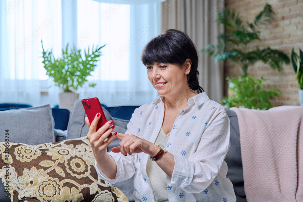 Mature woman sitting on sofa at home with smartphone
