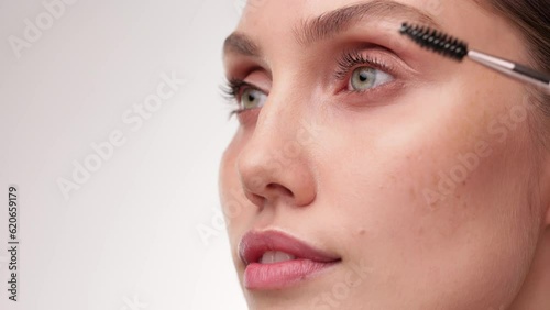 Beautiful girl scrubs her eyelashes looking at the camera and smiling. Beauty concept. Close up view. Brunette caucasian woman paints her eyebrows with eyebrow brush.