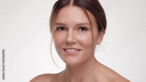 Close up Beauty face. Caucasian young woman look at the camera and smiling. Beautiful female with fresh glowing hydrated facial skin and natural makeup on light background at studio. Skin care concept