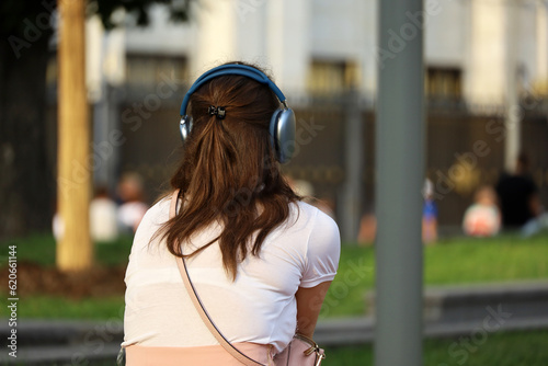 Girl with headphones sitting on summer street. Headset, listening to music and city life concept
