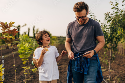 Happy son is walking with his father trough their orchard.