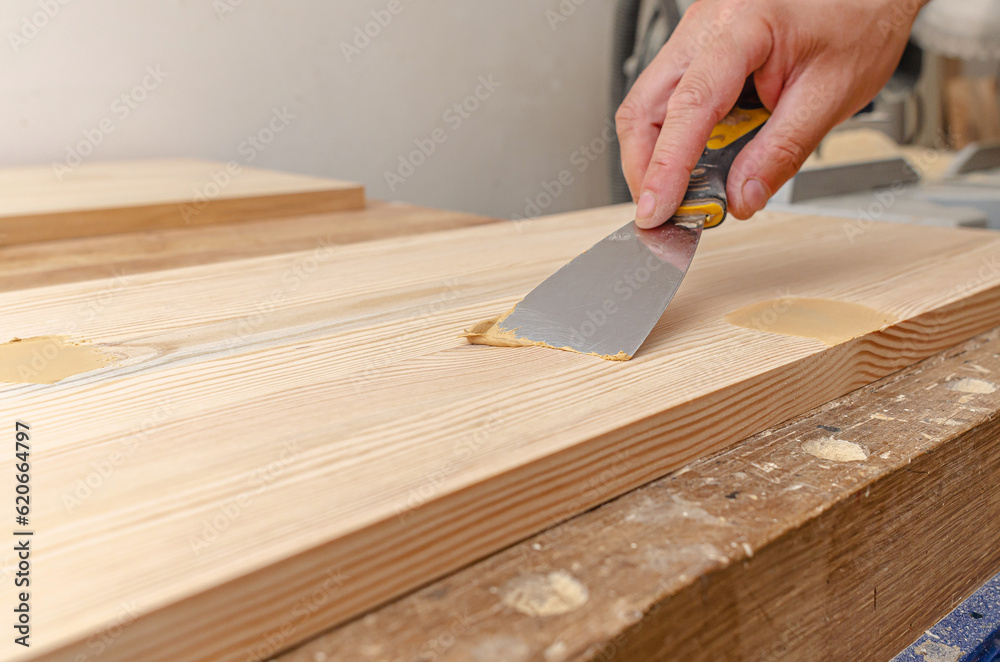 Covering knots on a wooden board with putty. Spatula, putty, wooden board. Carpenter's hands. Covering knots on a wooden board with putty. Spatula, putty, wooden board. Carpenter's hands.