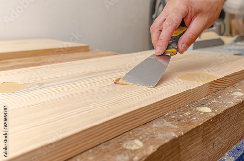 Covering knots on a wooden board with putty. Spatula, putty, wooden board. Carpenter's hands. photo