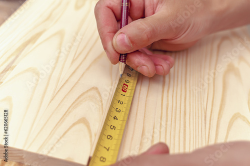 Carpenter's hand writes a marking with a pencil on a wooden board. Centimeter tape.