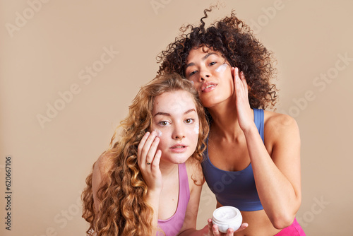 Delighted diverse female models applying cream on faces photo