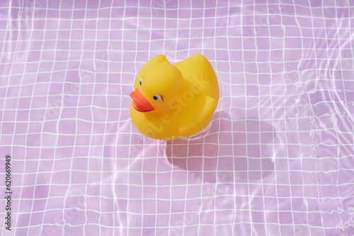 Yellow rubber ducky in pool water against pink tiles.