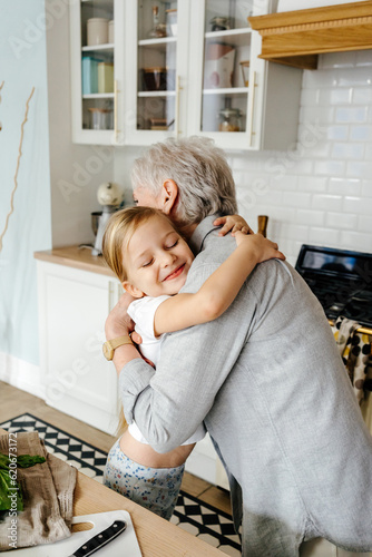 Cute girl hugging senior woman in kitchen with closed eyes