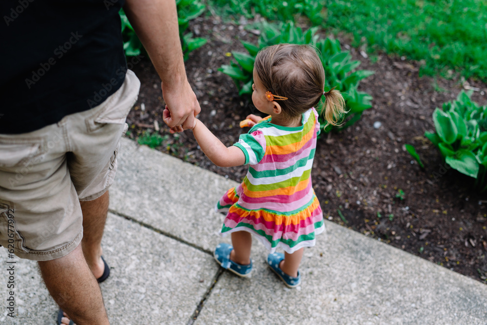 Father and daughter hold hands while walking
