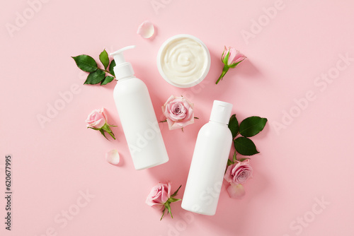 Set of natural cosmetics with roses flowers on pink background. Jar of cream, shower gel, shampoo bottle. Flat lay, top view.